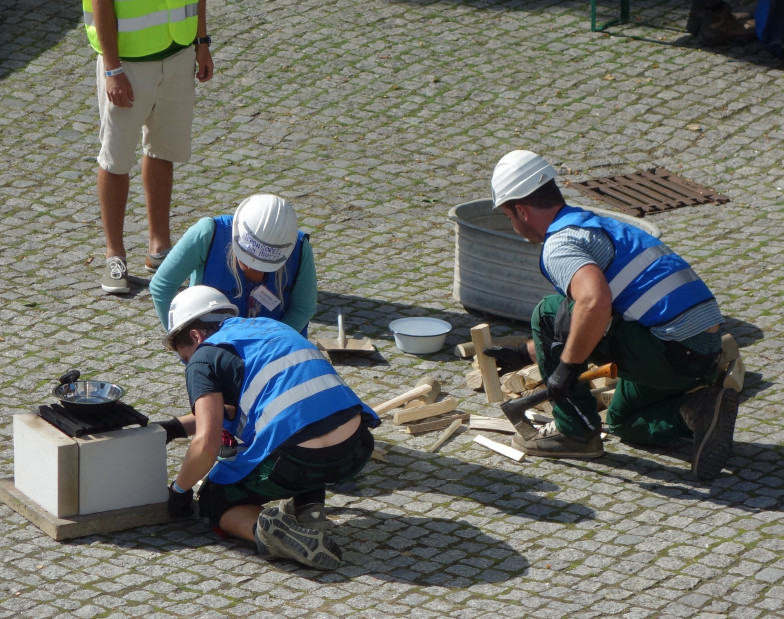 Foto: Drei Bauarbeiter knien auf Straßenpflaster und bauen eine Holzkiste