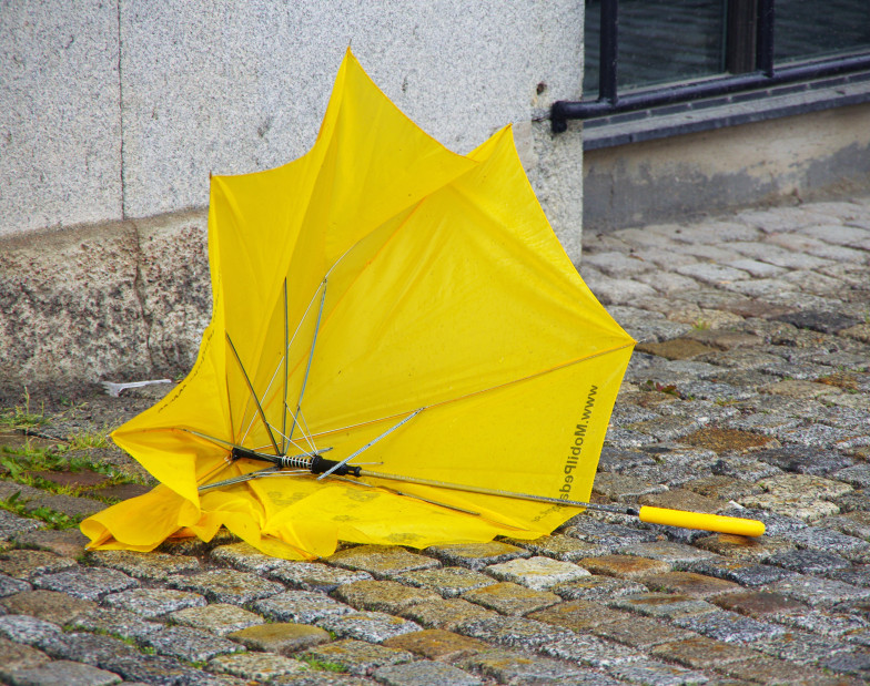 Foto: ein defekter gelber Regenschirm liegt auf dem Straßenpflaster