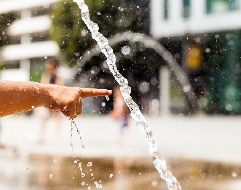 Hand zeigt auf Wasser am Springbrunnen. 