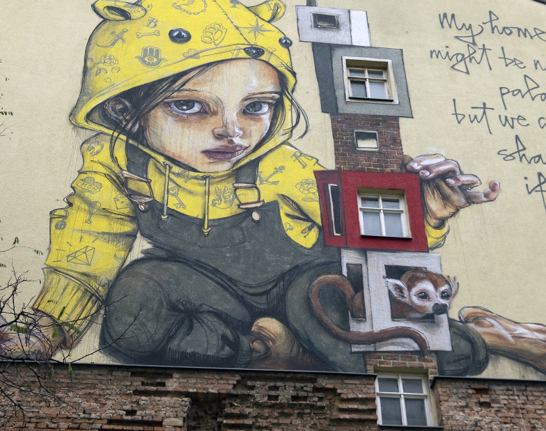 Foto: Streetart: Mädchen in gelbem Kapuzenpullover auf einer Hauswand