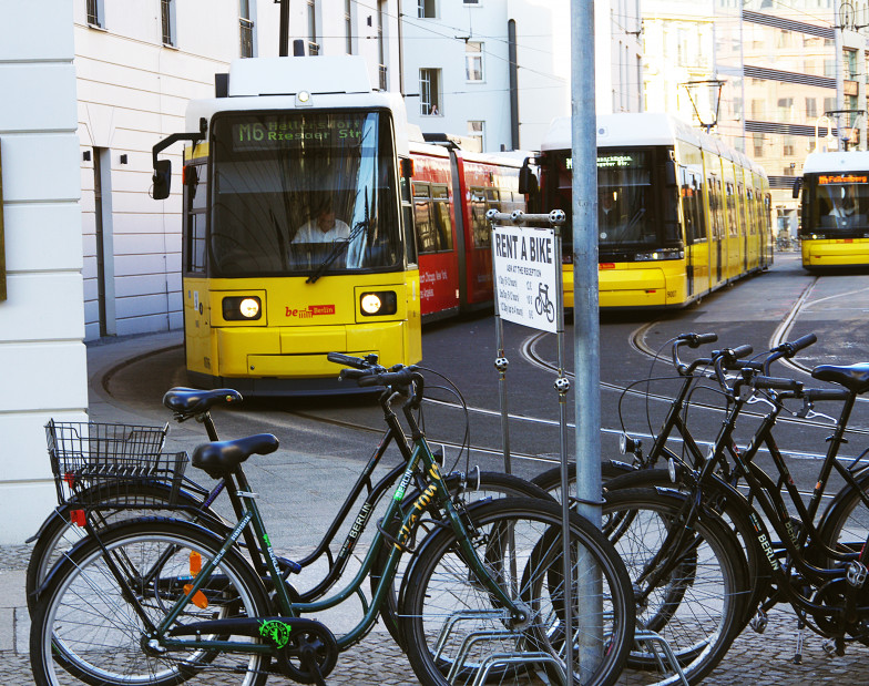 Foto von abgestellten Fahrrädern, im Hintergrund zwei Straßenbahnen