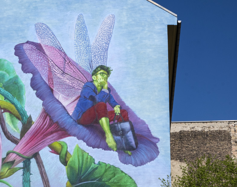 Foto: Streetart an einer Hausfassade: ein Mann mit Libellenflügeln sitzt in eine