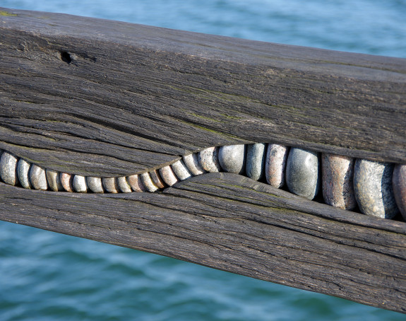 foto einer Holzplanke, in die zum Schmuck Ostseesteine eingelasen sind.