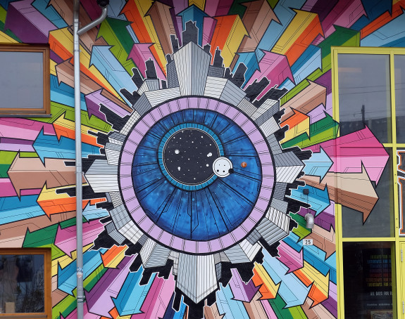 Foto eines Wandbildes: die Silhouette einer Stadt umgibt die Iris eines Auges