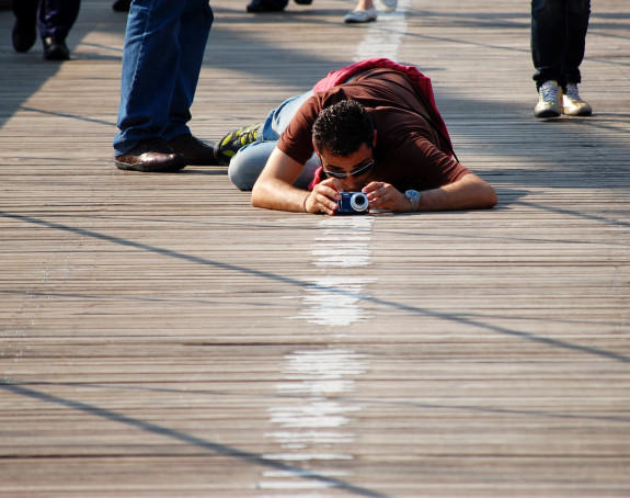 Photo: a man with a camera lies on the wooden planks of a bridge to take pictures