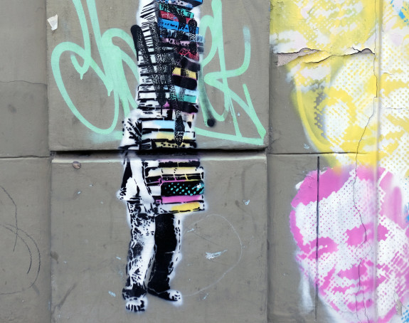 Foto: Graffito einer Person, die einen Bücherstapel schleppt und dahinter verborgen ist.