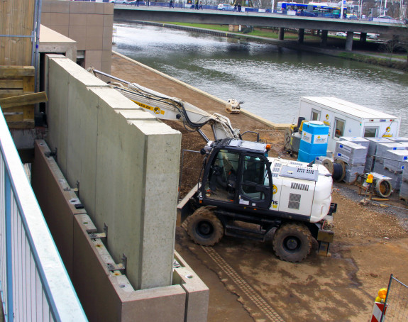 Foto einer Gewerbefläche. Zu sehen sind ein Bagger, Dämmmaterial, Container und eine Betonwand.