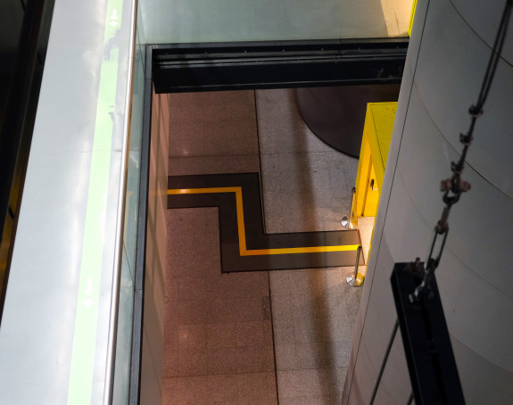 Foto: abstraktes Bild: von einer erhöhten Position aus wurde ein mit gelben Linine markierter Weg in einem Ausstellungsraum fotografiert
