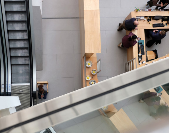 Foto: von einer erhöhten Position aus wurde ein Raum mit Menschen an einem Tresen und einer Rolltreppe fotografiert