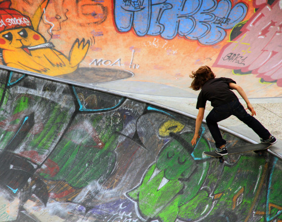 Foto: ein Junge auf einem Skateboard fährt auf einer mit Graffiti besprühten Bahn