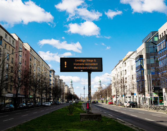 Foto:Straße vierspurig, in der Mitte ein Screen "Unnötige Wege und Kontakte vermeiden"  