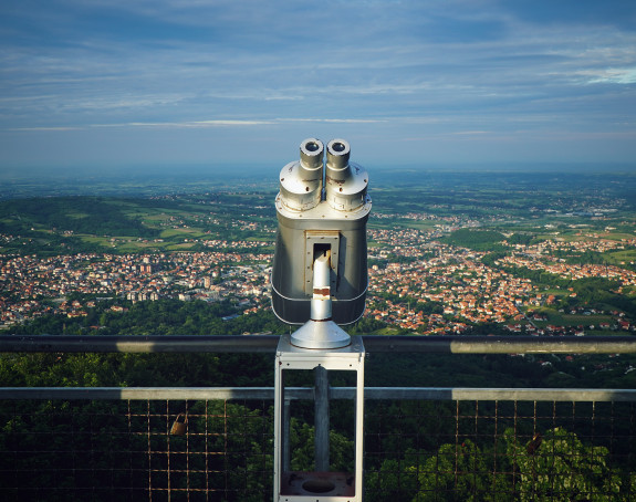 Fernglas in der Mitte des Bildes zeigt auf ein Tal in dem eine Stadt liegt.