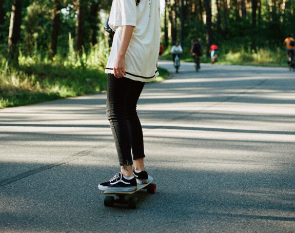 Frau auf einem Skateboard, Radfahrende im Hintergrund
