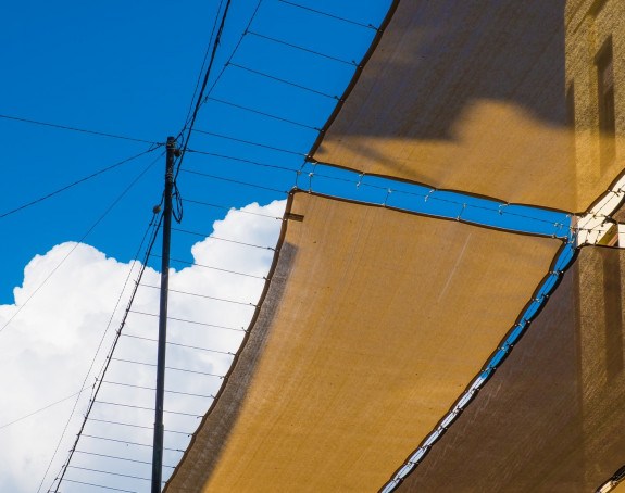 an Häusern befestigte Sonnensegel vor einem blauen Himmel