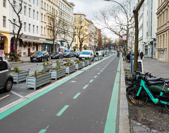 Das Foto zeigt den neuen Fahrradweg in der Bergmannstraße, Berlin, daneben Pflanzkübel, parkende Autos, Leihräder und der Gehweg.