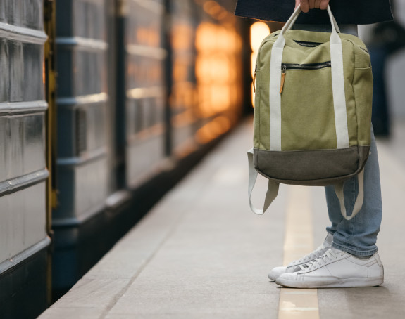 Bahngleis mit vorfahrender Bahn und Nahaufnahme der Füße eines Passanten mit Rucksack.