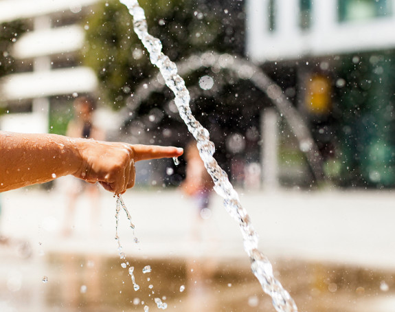 Hand zeigt auf Wasser am Springbrunnen.