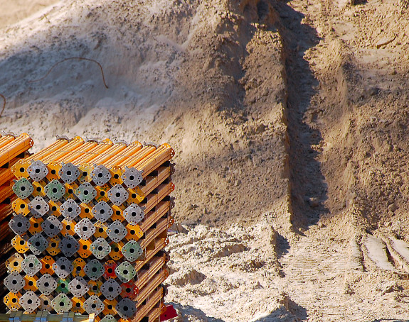 Foto: eine Baugrube mit gelben Metallbauteilen und einem Sandberg im Hintergrund