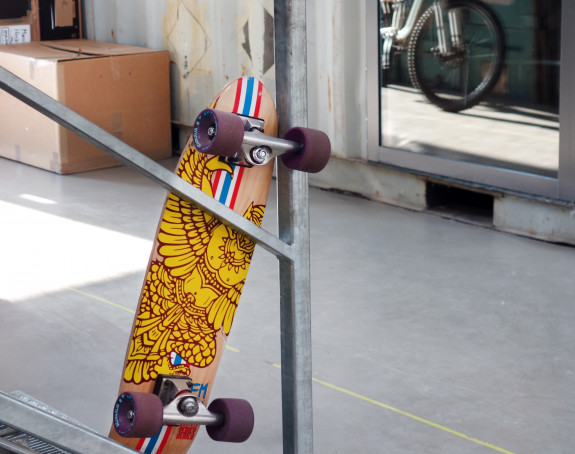 Foto: ein farbiges Skateboard lehnt an einem Metallgitter