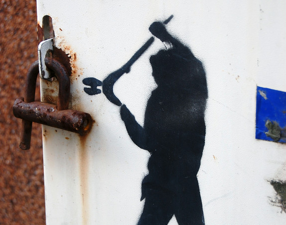 Foto Streetart: eine gesprayte Person knackt ein reales Vorhängeschloss