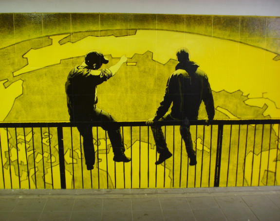 Foto: zwei Männer auf einem Geländer, einer zeigt auf die Abbildung der Erde