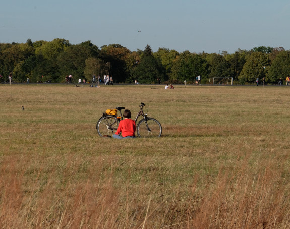 Foto: Eine Frau sitzt auf einer großen Wiese, vor sich ihr Fahrrad.