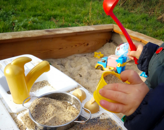 Foto: Buddelkiste mit Kinderspielzeug und eine Kinderhand mit Sandförmchen